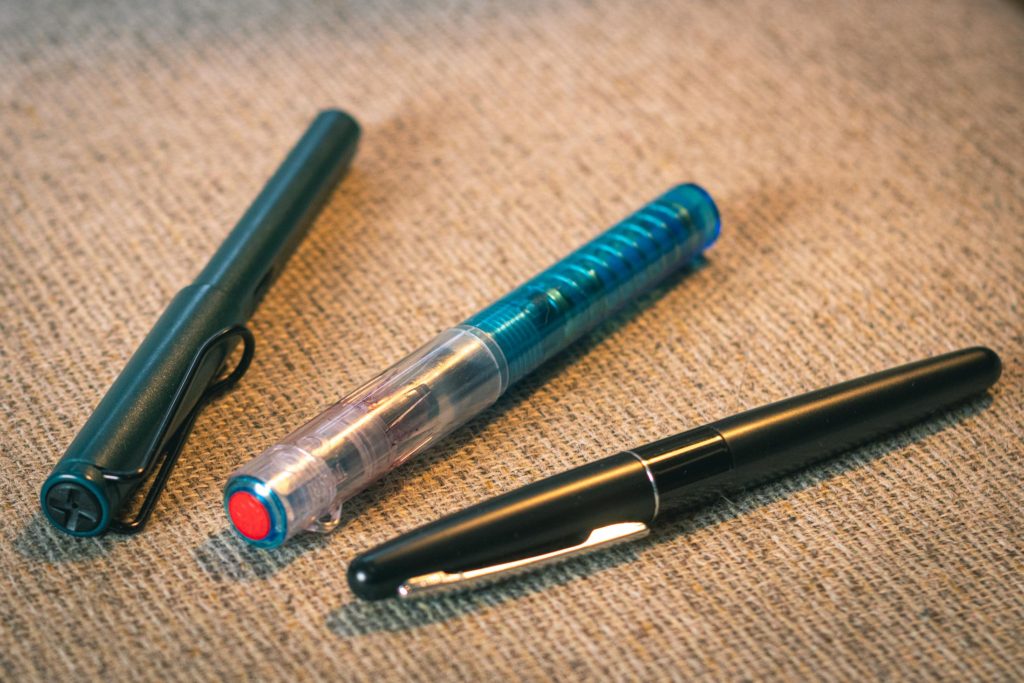 Photo de trois stylo plume d'entrée de gamme, un Lamy Safary Petrol, un TWSBI GO bleu, un Pilot Metrolpolitan